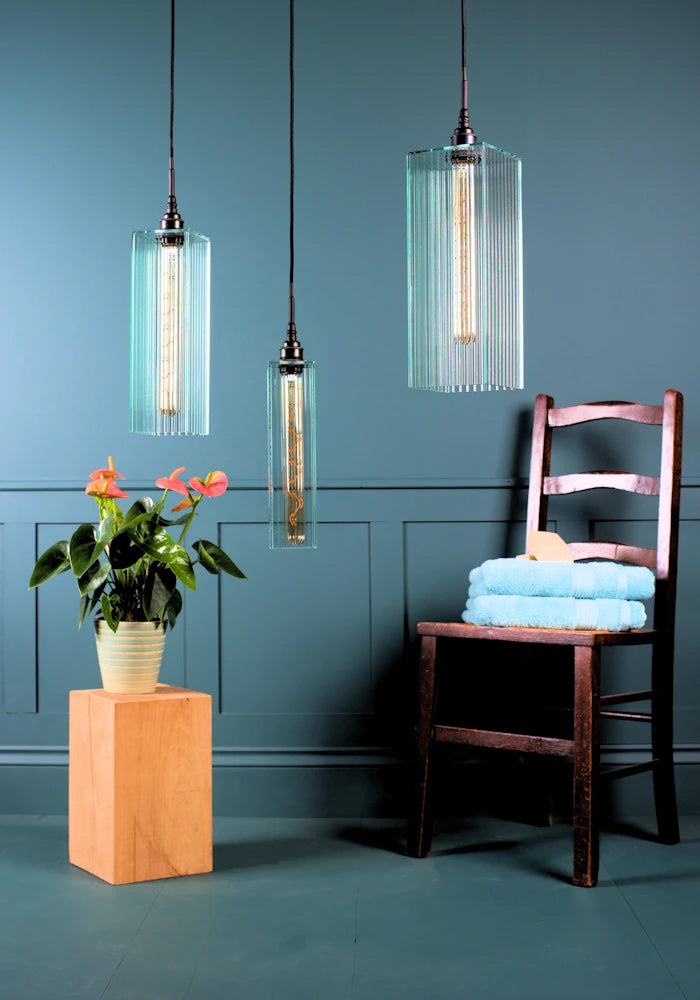 Triple large ribbed glass bathroom pendant light cluster switched off with plant, wooden chair and towels.