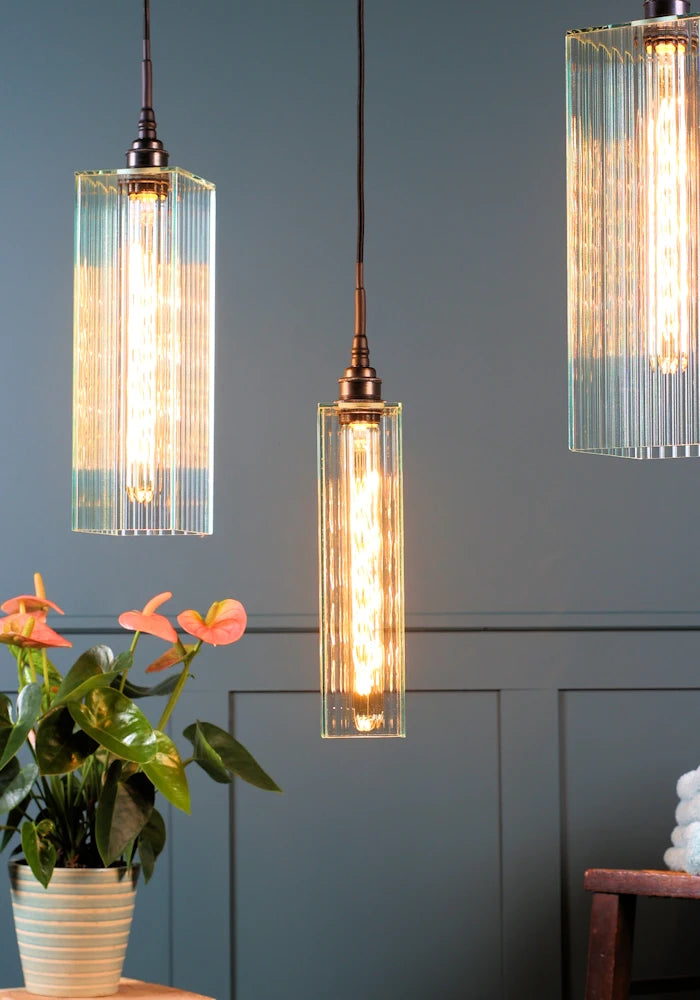 Close up of triple large ribbed glass bathroom pendant light cluster with plant.