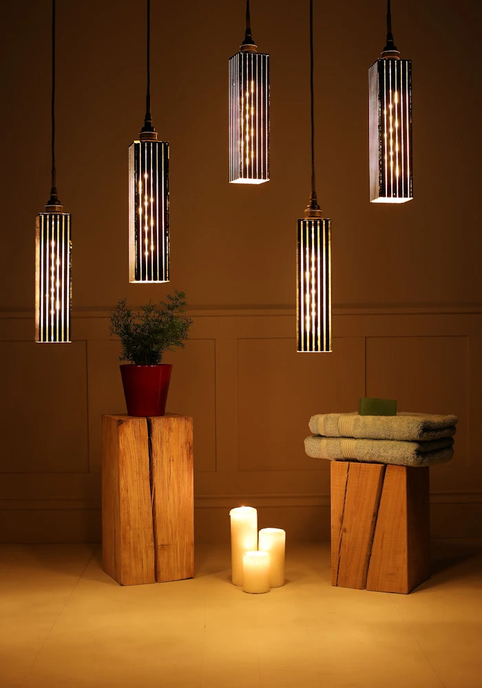 5 black and gold cluster bathroom pendant light casting shadows on plant, candles and bath towels.