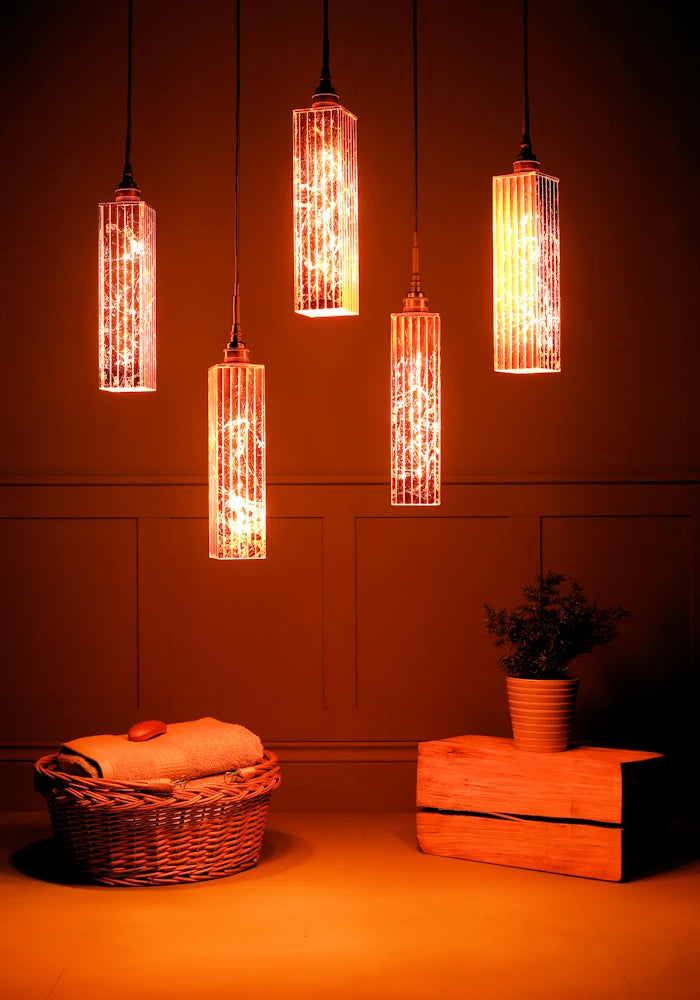 Cluster of five long rectangular copper leaf bathroom pendant lights casting shadows, basket of bath towels and plant.