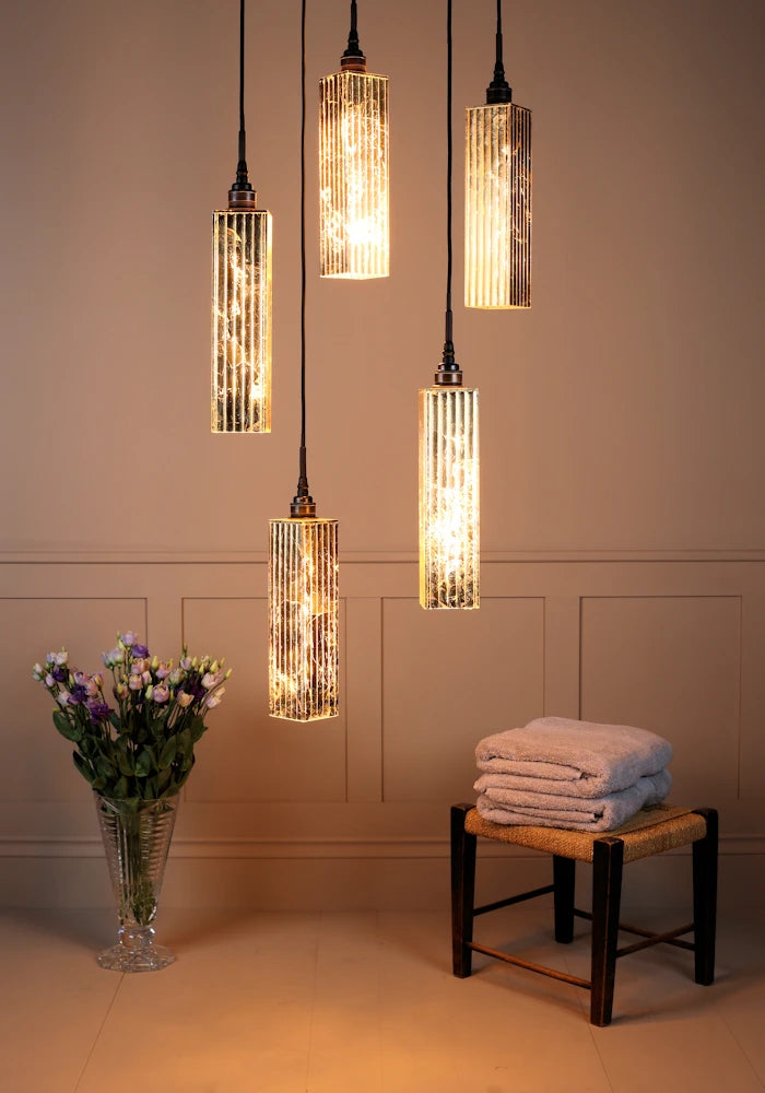 5 cluster gold leaf rectangular bathroom pendant lights with vase of flowers and bath towels.