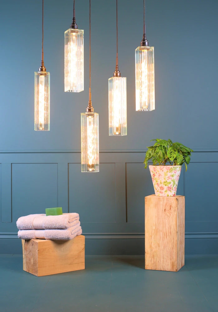 Five long rectangular ribbed glass cluster bathroom pendant lights with bath towels and pot plant.