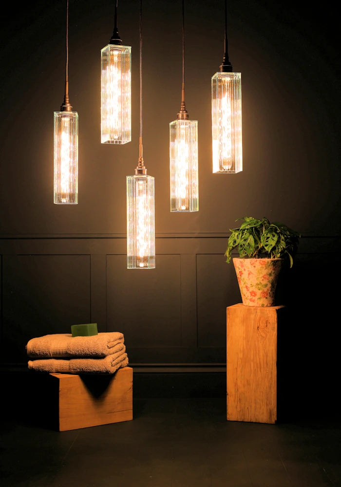 Five long rectangular ribbed glass cluster bathroom pendant lights with bath towels and pot plant.