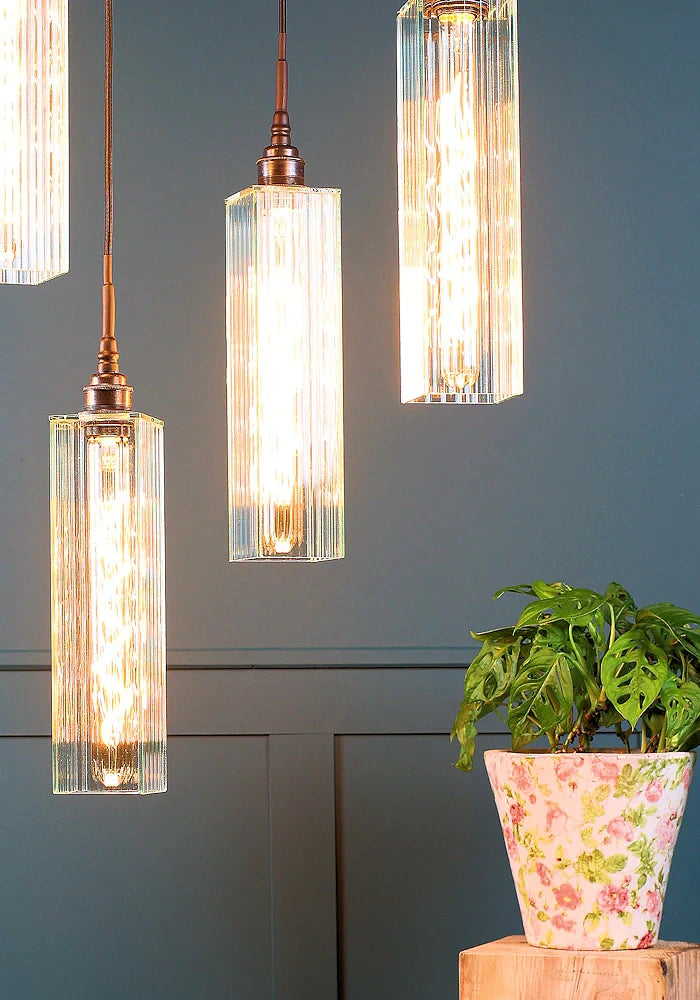 Close up of long rectangular ribbed glass cluster bathroom pendant lights with pot plant.