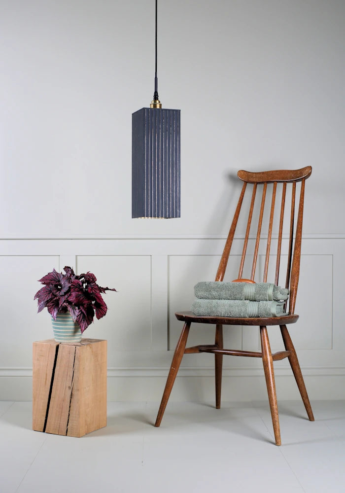 Large black and gold rectangular bathroom pendant light switched off with plant, wooden chair and bath towels.