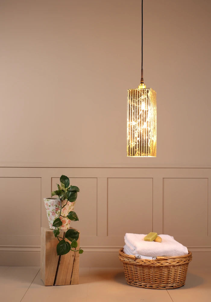 Large rectangular gold leaf bathroom pendant light with plant and bath towels in basket.