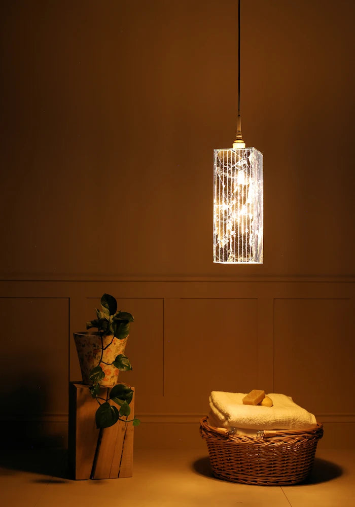 Large rectangular gold leaf bathroom pendant light casting shadows onto plant and bath towels in basket.