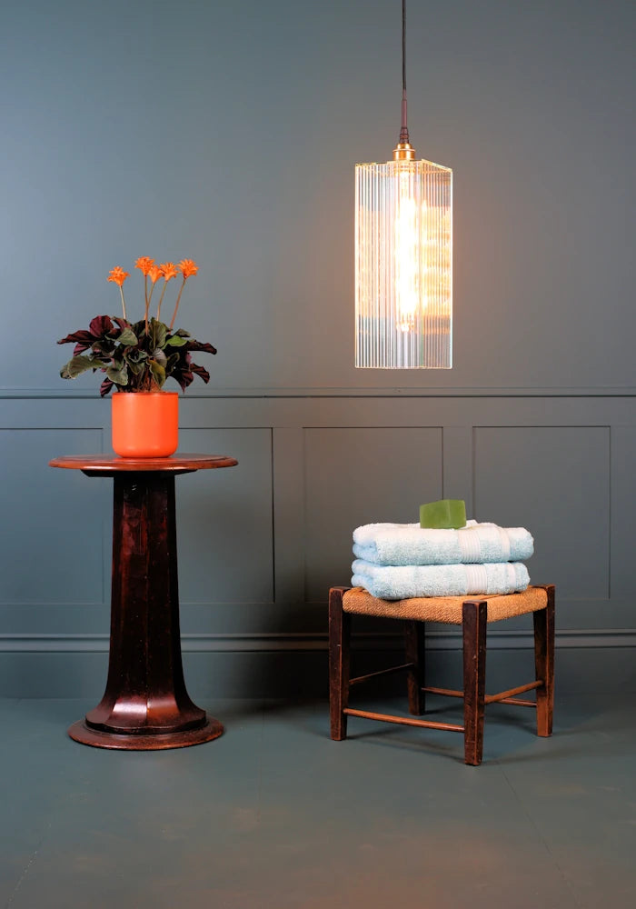 Large rectangular ribbed glass bathroom pendant light with orange plant and bath towels.