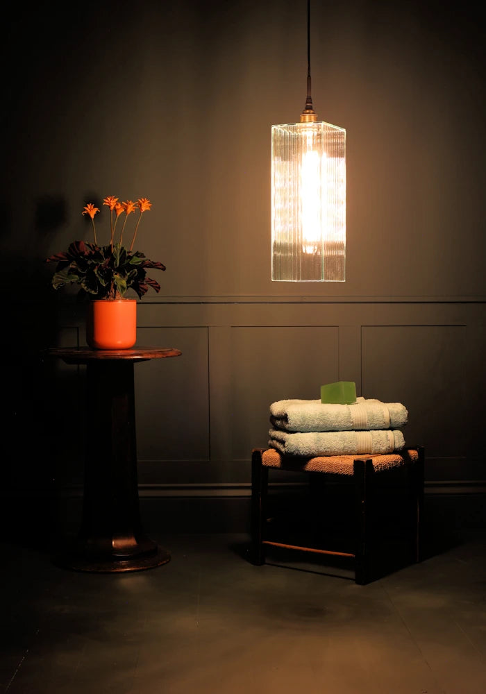 Large rectangular ribbed glass bathroom pendant light with orange plant and bath towels.