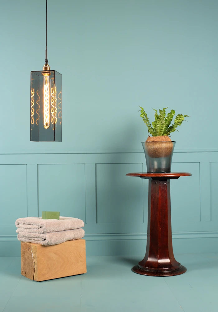 Large rectangular smoked glass bathroom pendant light, bath towels and plant.