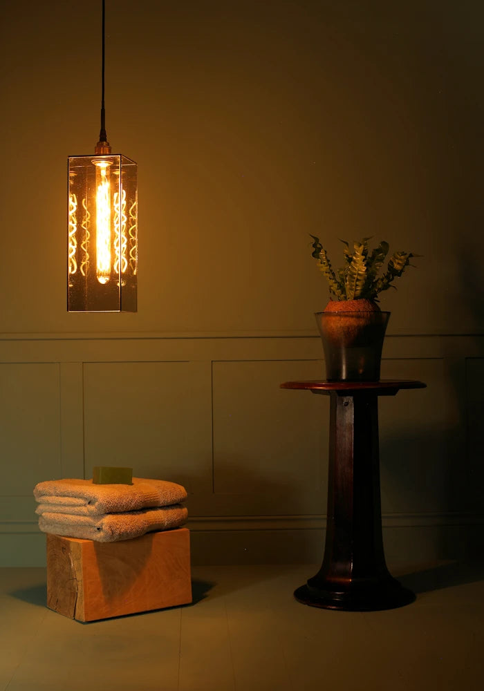 Large rectangular smoked glass bathroom pendant light casting shadows, bath towels and plant.