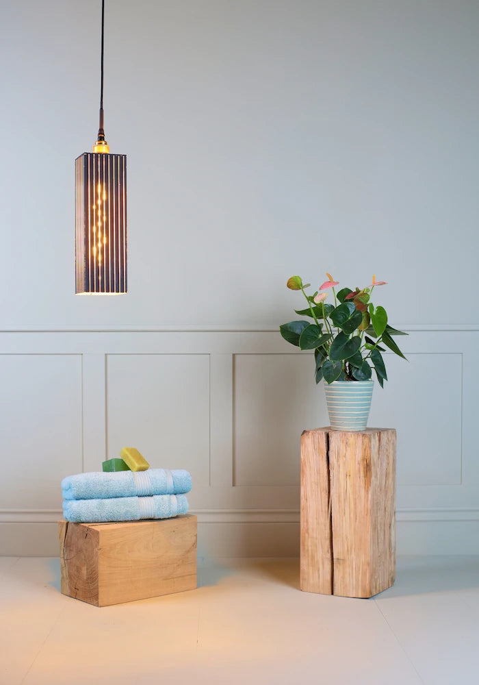 Black and gold leaf large bathroom pendant light with bath towels and pot plant on wooden block.