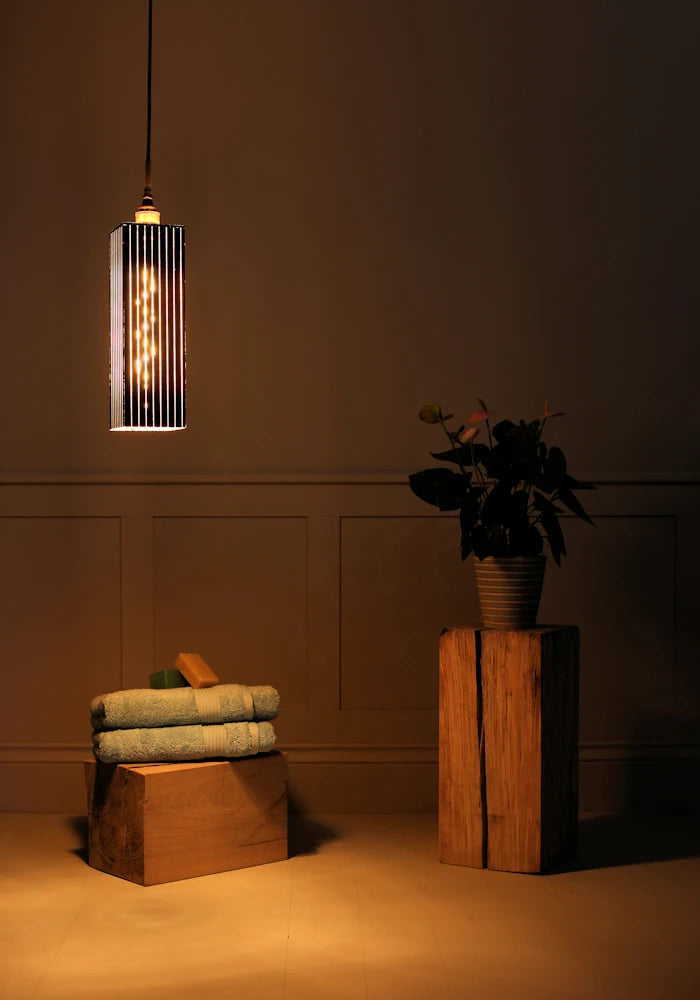 Black and gold leaf large bathroom pendant light with bath towels and pot plant on wooden block.