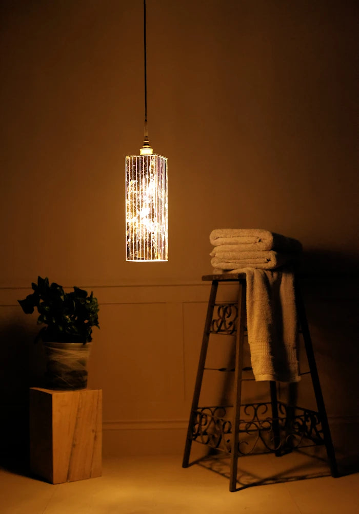 Long rectangular gold leaf bathroom pendant light casting shadows onto bath towels and plant.