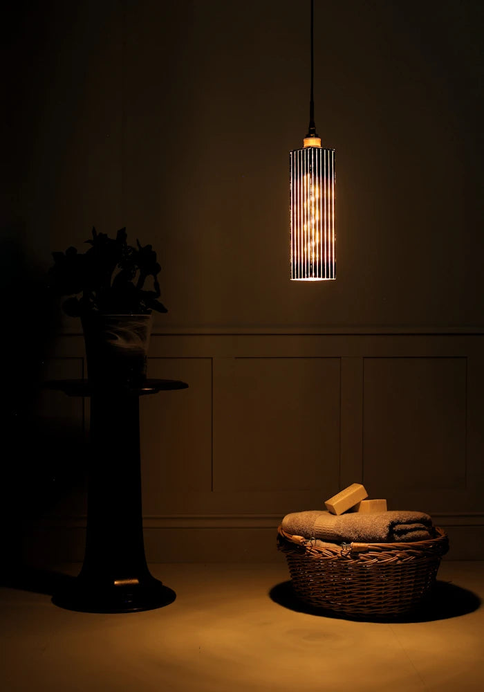 Elegant long rectangular black and gold bathroom pendant light casting shadows onto plant and basket of bath towels.