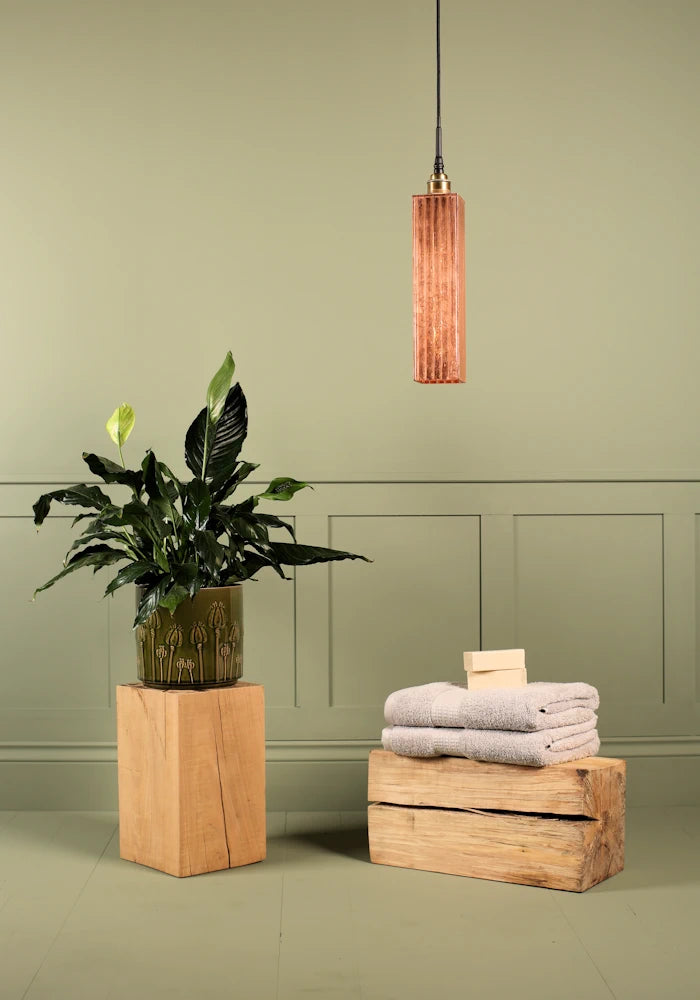 Elongated copper leaf bathroom pendant light switched off, plant and bath towels.