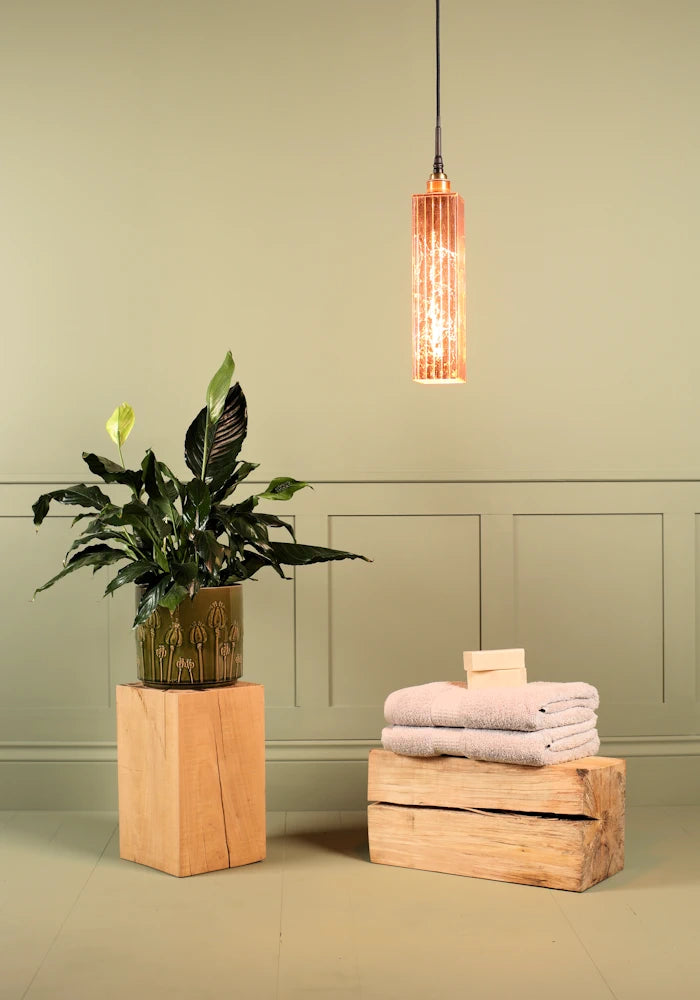 Elongated copper leaf bathroom pendant light, plant and bath towels.