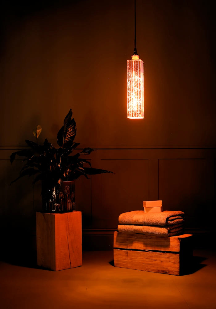 Elongated copper leaf bathroom pendant light casting shadows, plant and bath towels.