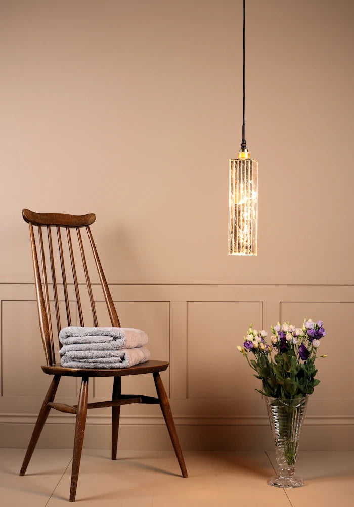 Long rectangular gold leaf bathroom pendant light with bath towels on wooden chair and vase of flowers.