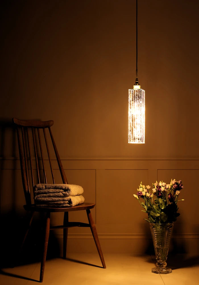 Long rectangular gold leaf bathroom pendant light with bath towels on wooden chair and vase of flowers.