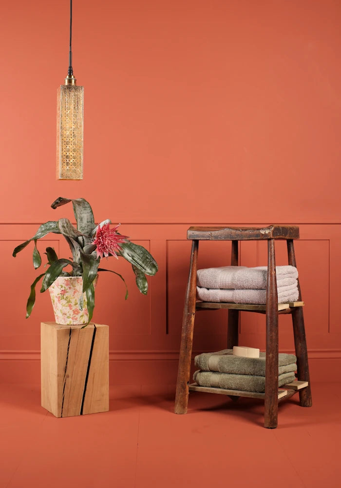 Elongated rectangular Moroccan style bathroom pendant light switched off, plant and wooden stool with bath towels.