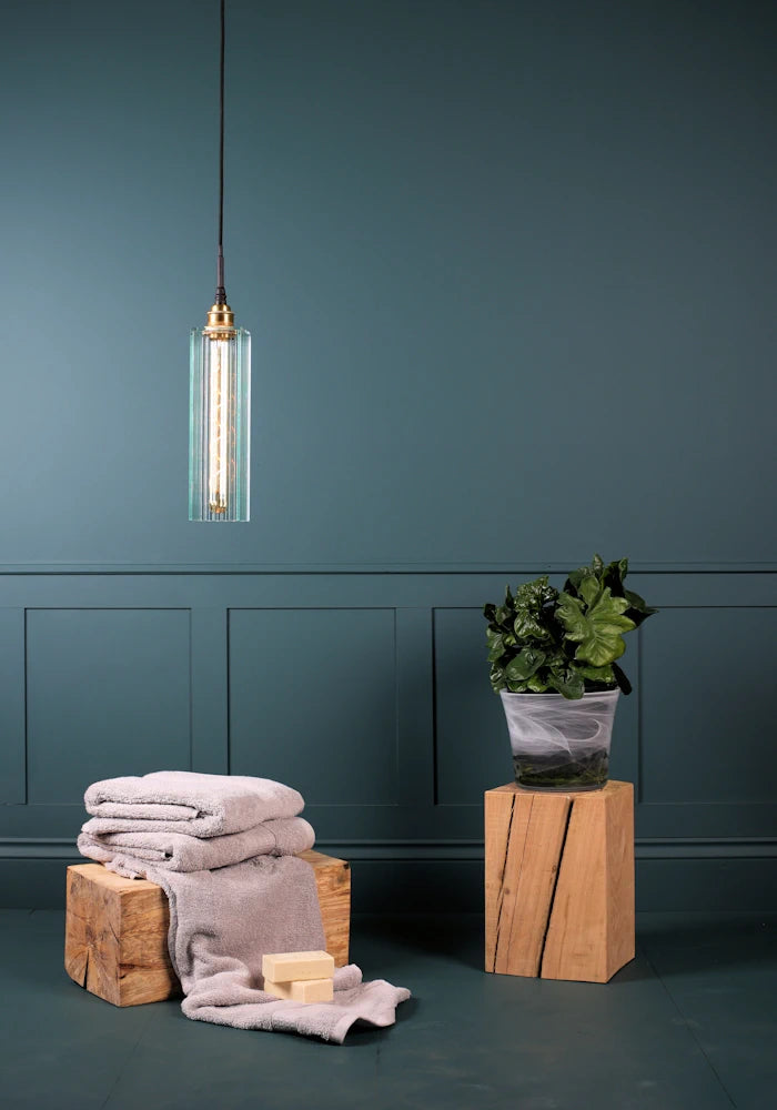 Long rectangular ribbed glass bathroom pendant light switched off with bath towels and plant.