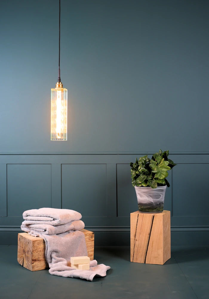 Long rectangular ribbed glass bathroom pendant light with bath towels and plant.