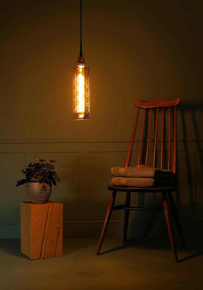 Elongated rectangular smoked glass bathroom pendant light, plant, wooden chair and bath towels.